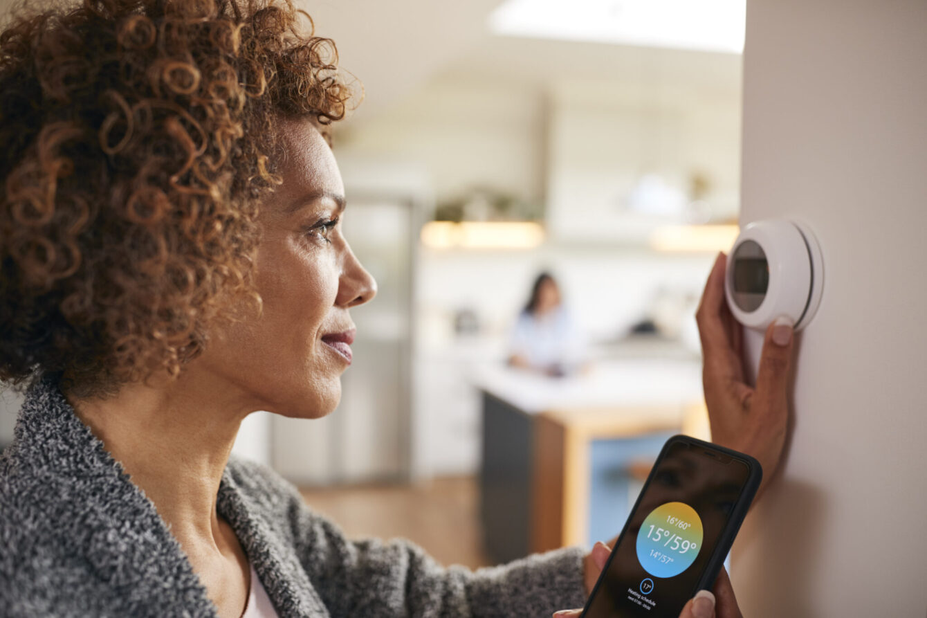 Mature woman using her phone app to control her digital central heating thermostat.