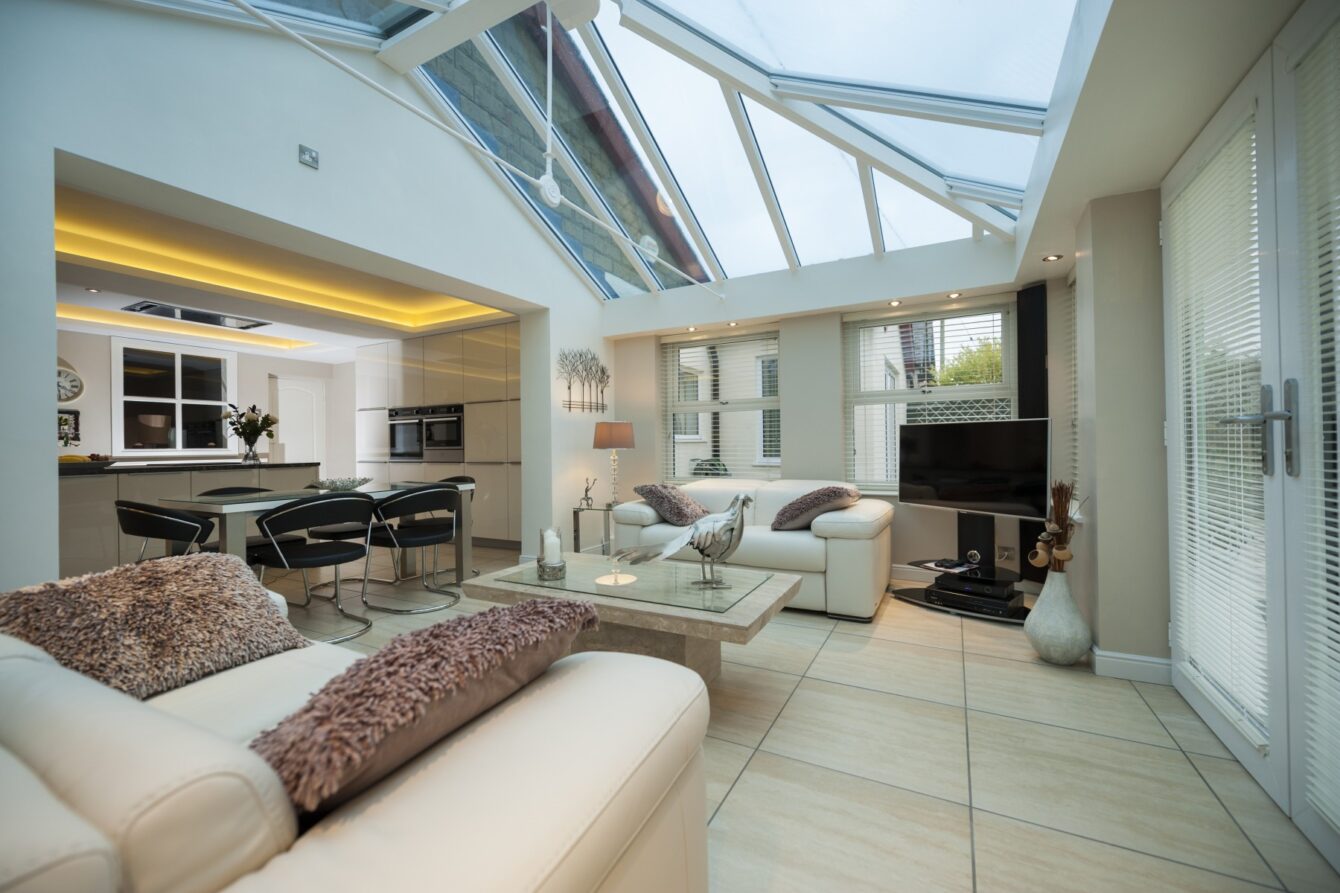 A modern conservatory with cream and beige décor and a tiled floor featuring a glazed pitched roof.