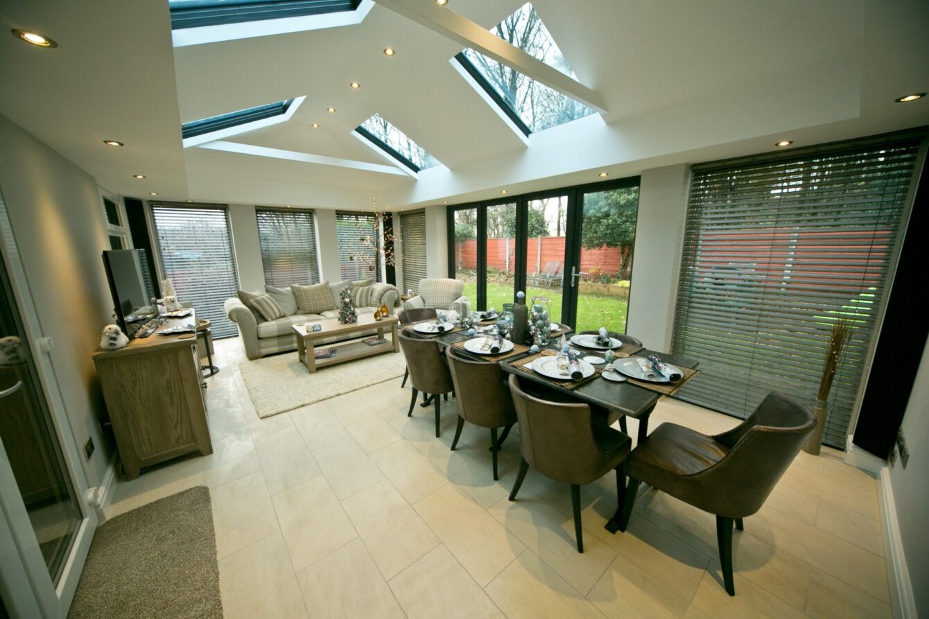 A large, tiled conservatory with a principally enclosed roof with four large skylights. The inside features a dining table with chairs plus a comfortable living space.