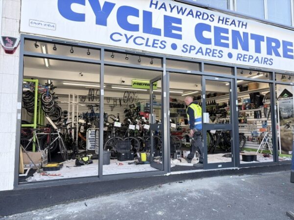 Haywards Heath Cycle Centre shopfront with window frames and no glass, a workman in a high-vis vest is inside. 