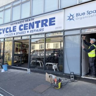 Haywards Heath Cycle Centre shopfront showing Blue Spark Organisation next door with a workman in a high-vis vest working in the doorway.