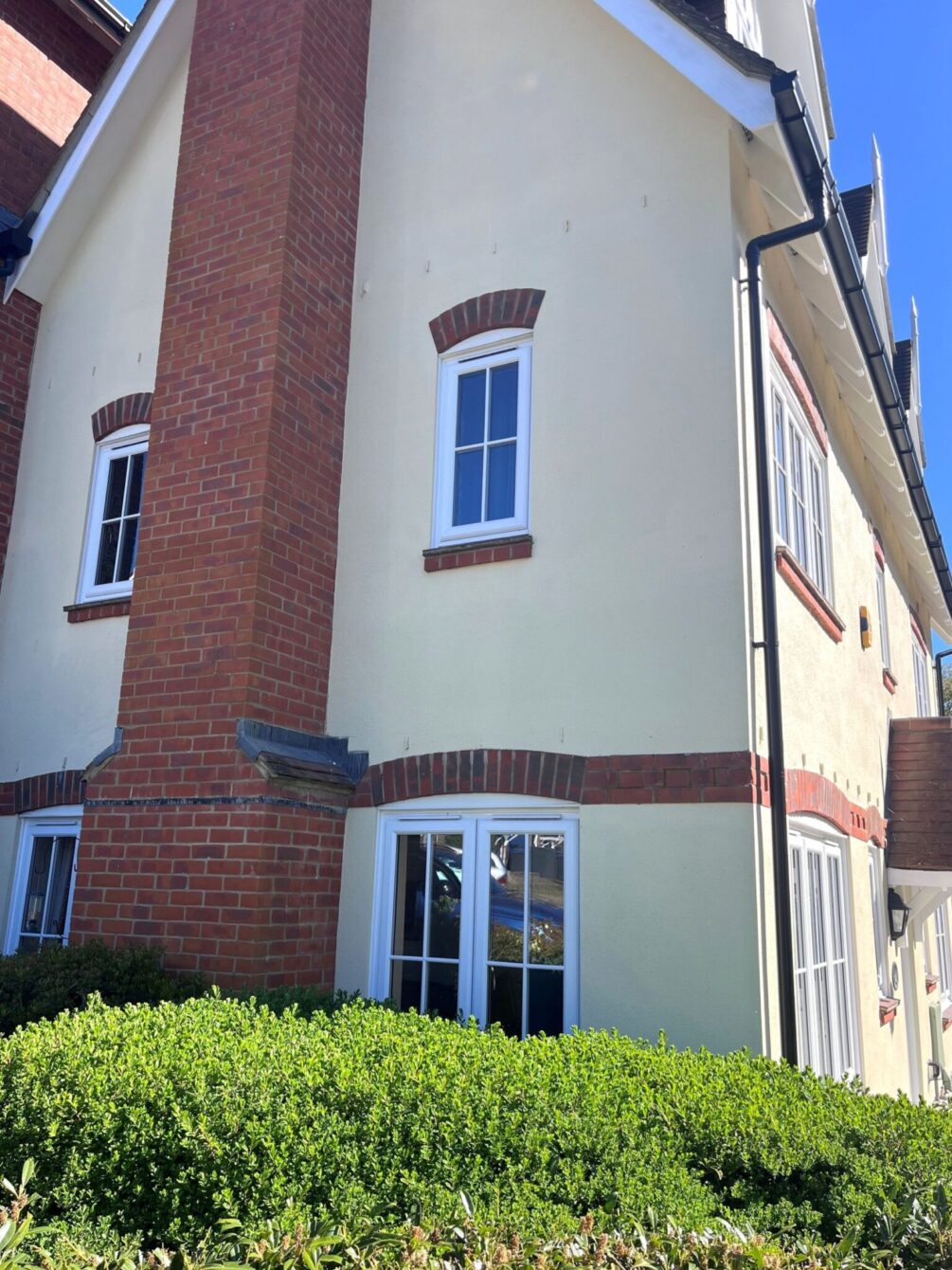 Side view of a cream rendered house with new PVCu sliding sash windows. There is a brick chimney stack in the centre of the building.