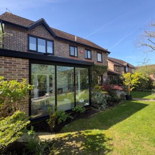 A house with a modern hup! extension to the back with three large windows and a closed-in section with brick-effect panelling to match the house. It overlooks a spacious mature garden.