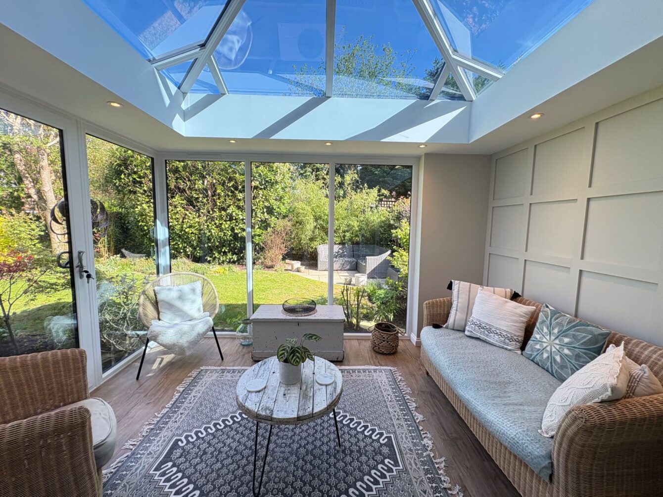 Inside the hup! extension looking out to the garden. Inside there is a panelled wall to the right with a rattan sofa, coffee table and two conservatory chairs.
